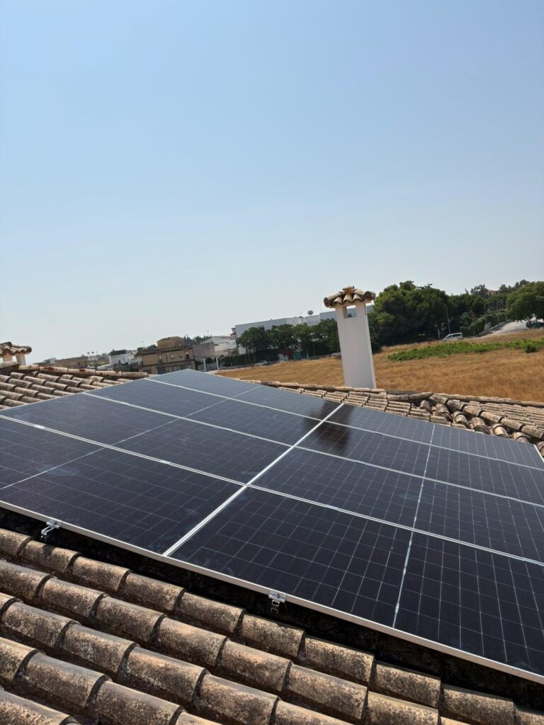 Placas solares instaladas sobre teja envejecida, con el campo al fondo