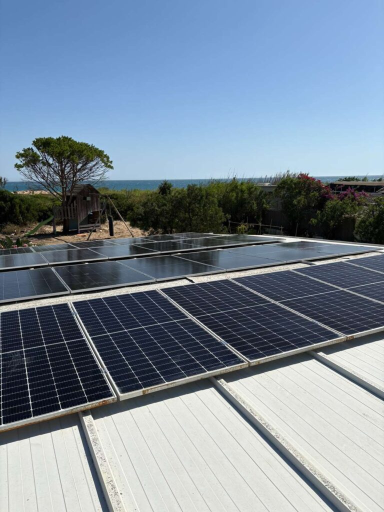 Paneles solares sobre cubierta blanca frente al mar, entre pinos