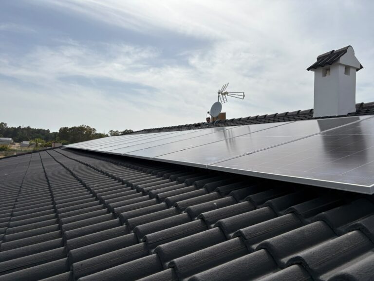 Paneles solares en un tejado de teja negra, junto a la antena
