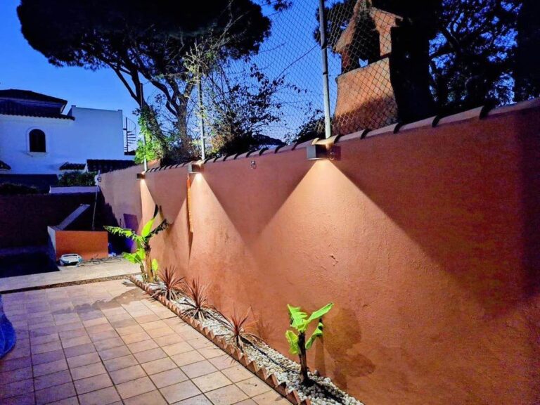 Iluminación exterior encendida en el muro de un jardín, de noche