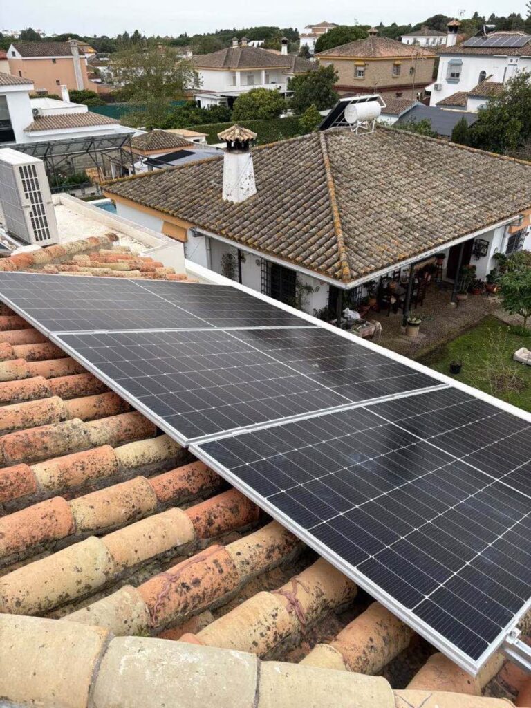 Paneles solares sobre teja envejecida, con el patio de la casa al fondo