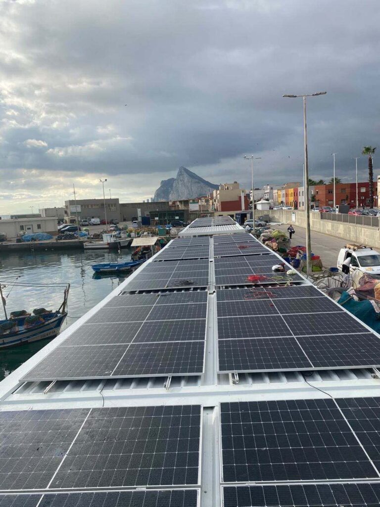 Paneles solares en la cubierta de una nave del puerto, con el Peñón al fondo